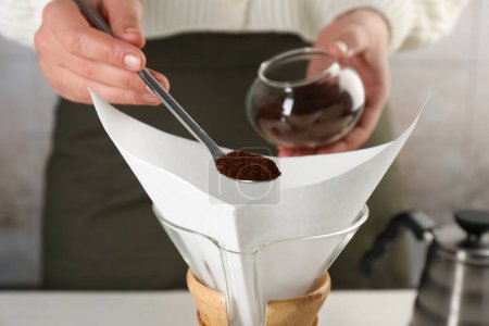 Foto de Haciendo café por goteo. Mujer añadiendo café molido en la cafetera chemex con filtro de papel, primer plano - Imagen libre de derechos