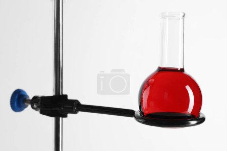 Retort stand and laboratory flask with liquid on white background, closeup
