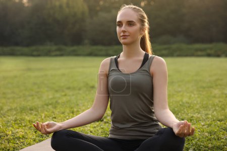 Téléchargez les photos : Belle femme pratiquant le yoga dans le parc. Pose de lotus - en image libre de droit