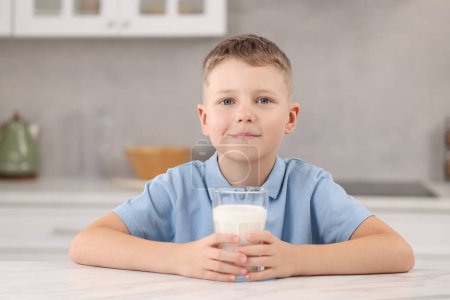 Téléchargez les photos : Garçon mignon avec verre de lait à la table blanche dans la cuisine - en image libre de droit