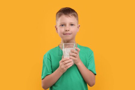 Téléchargez les photos : Mignon garçon avec un verre de lait frais sur fond orange - en image libre de droit