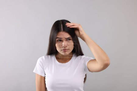 Téléchargez les photos : Femme émotionnelle examinant ses cheveux et son cuir chevelu sur fond gris - en image libre de droit