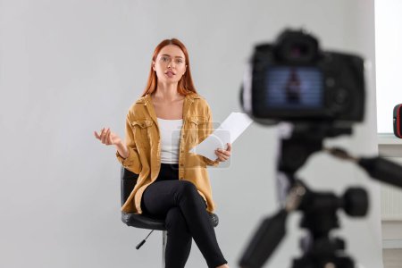 Casting call. Young woman with script performing in front of camera against light grey background at studio
