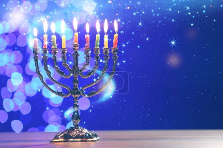 Téléchargez les photos : Hanoukka fête. Menorah avec des bougies allumées sur table en bois sur fond bleu avec des lumières floues, espace pour le texte - en image libre de droit