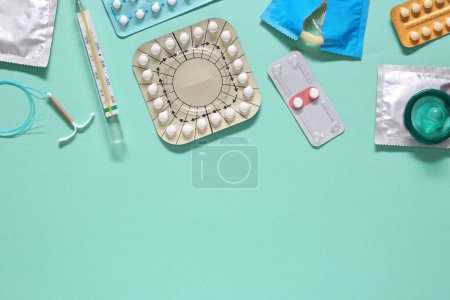 Contraceptive pills, condoms, intrauterine device and thermometer on turquoise background, flat lay with space for text. Different birth control methods