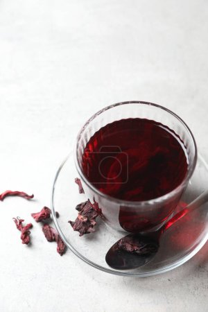 Aromatic hibiscus tea in glass, dried roselle calyces and spoon on light table, above view