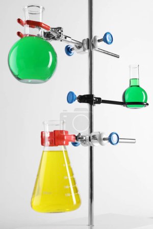 Retort stand and laboratory flasks with liquids on white background