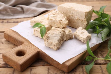 Pieces of tasty halva and mint leaves on wooden table, closeup