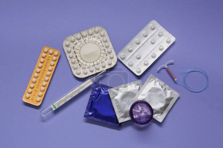 Contraceptive pills, condoms, intrauterine device and thermometer on violet background, flat lay. Different birth control methods