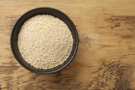 Dry quinoa seeds in bowl on wooden table, top view. Space for text