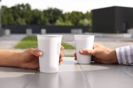 Téléchargez les photos : Café à emporter. Couple avec gobelets en papier à table à l'extérieur, mise au point sélective - en image libre de droit