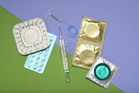 Contraceptive pills, condoms, intrauterine device and thermometer on color background, flat lay. Choice of birth control method