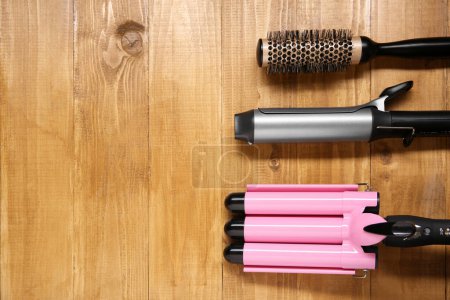 Téléchargez les photos : Différents fers à friser les cheveux et brosse ronde sur fond en bois, pose plate. Espace pour le texte - en image libre de droit