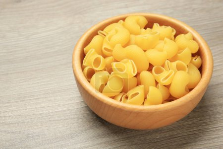 Raw macaroni pasta in bowl on light grey wooden table, closeup. Space for text