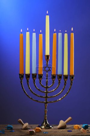 Téléchargez les photos : Hanoukka fête. Menorah avec des bougies brûlantes et des dreidels sur une table en bois sur fond bleu - en image libre de droit