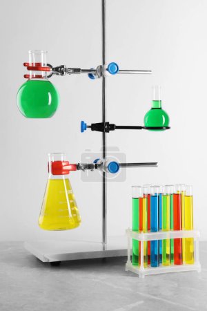 Retort stand and laboratory glassware with liquids on grey table against white background