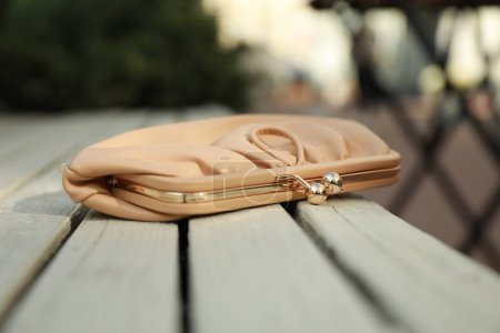 Beige leather purse on wooden bench outdoors, closeup. Lost and found