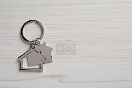 Metal keychain in shape of houses on white wooden table, top view. Space for text