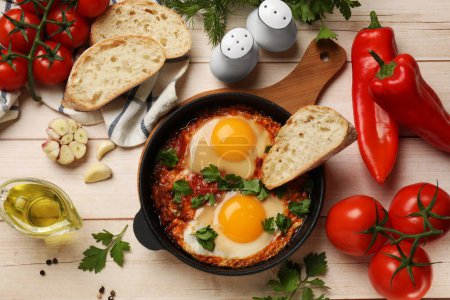 Flat lay composition with delicious shakshuka in frying pan on light wooden table