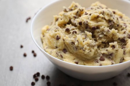 Chocolate chip cookie dough in bowl on light gray table, closeup