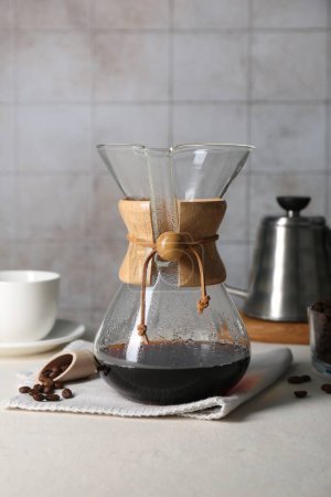 Glass chemex coffeemaker with tasty drip coffee and beans on white table