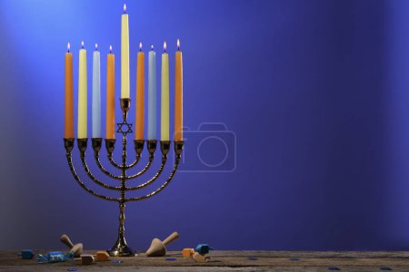 Téléchargez les photos : Hanoukka fête. Menorah avec des bougies brûlantes et des dreidels sur table en bois sur fond bleu, espace pour le texte - en image libre de droit