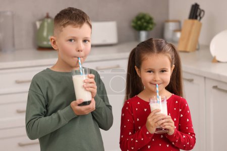 Téléchargez les photos : Enfants mignons boire du lait frais à partir de verres dans la cuisine - en image libre de droit