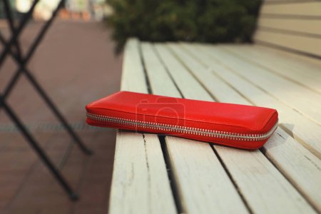 Red purse on wooden bench outdoors, closeup. Lost and found