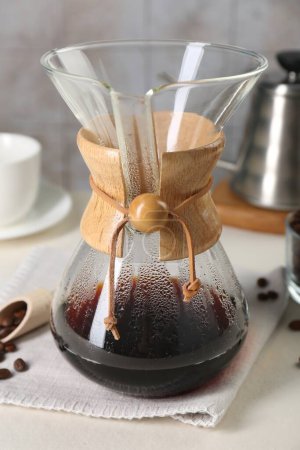 Glass chemex coffeemaker with tasty drip coffee and beans on white table, closeup