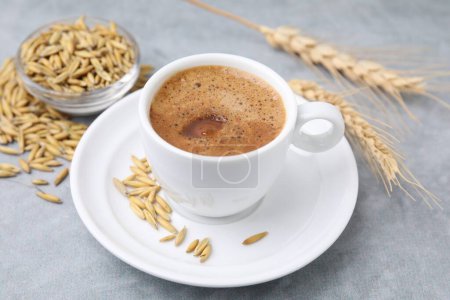 Cup of barley coffee, grains and spikes on gray table, closeup