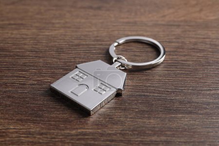 Metal keychain in shape of house on wooden table, closeup