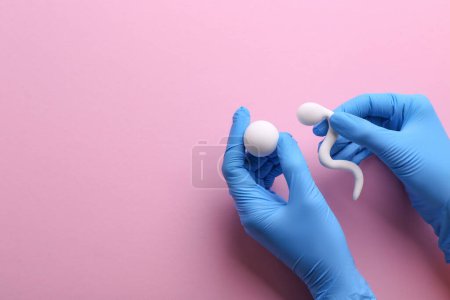 Reproduktionsmedizin. Fruchtbarkeitsspezialist in Handschuhen mit Figuren von Spermien und Eizellen auf rosa Hintergrund, Draufsicht mit Platz für Text