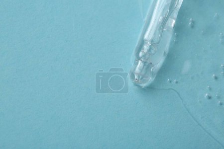 Photo for Dripping cosmetic serum from pipette onto light blue background, top view. Space for text - Royalty Free Image