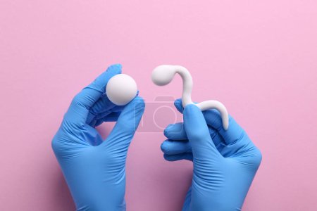 Foto de Medicina reproductiva. Fertilidad especialista en guantes que sostiene figuras de espermatozoides y óvulos sobre fondo rosa, vista superior - Imagen libre de derechos