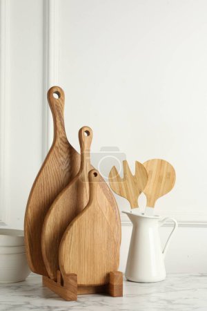 Foto de Tableros de madera para cortar, utensilios de cocina y vajilla sobre mesa de mármol blanco - Imagen libre de derechos