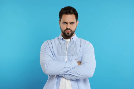 Photo for Portrait of resentful man with crossed arms on light blue background - Royalty Free Image