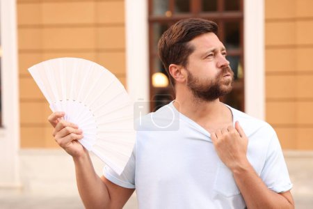 Homme avec ventilateur à main souffrant de chaleur à l'extérieur