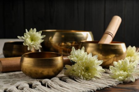 Tibetan singing bowls with beautiful flowers and mallet on wooden table
