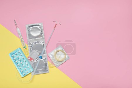 Contraceptive pills, condoms, intrauterine device and thermometer on color background, flat lay with space for text. Choice of birth control method