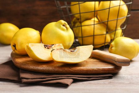 Ripe whole and cut quinces with knife on wooden table, closeup