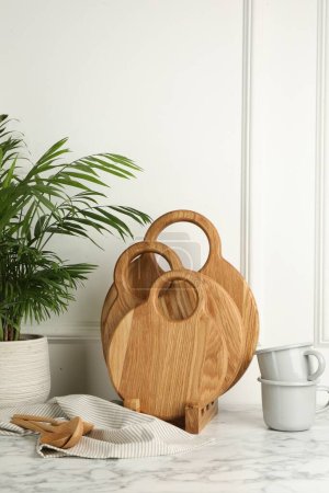 Foto de Tableros de corte de madera, cucharas, vajilla y planta de interior sobre mesa de mármol blanco - Imagen libre de derechos