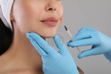 Doctor giving facial injection to young woman on light grey background, closeup. Cosmetic surgery