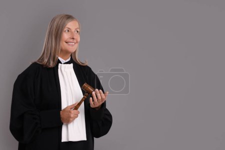 Smiling senior judge with gavel on grey background. Space for text