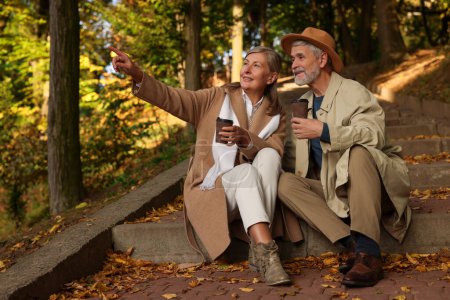 Téléchargez les photos : Couple sénior affectueux avec des tasses de café passer du temps ensemble dans le parc d'automne - en image libre de droit