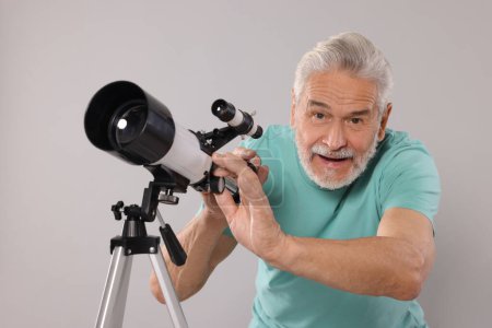 Senior astronomer with telescope on grey background