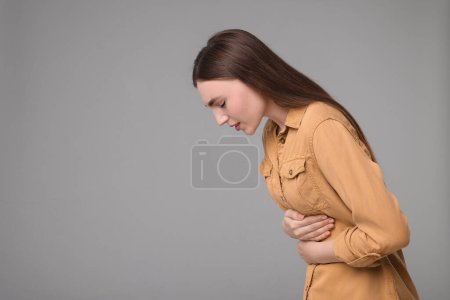Foto de Mujer joven que sufre de dolor de estómago sobre fondo gris. Espacio para texto - Imagen libre de derechos