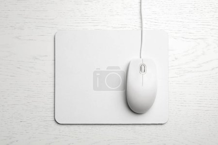 Wired computer mouse and pad on white wooden background, flat lay. Space for text