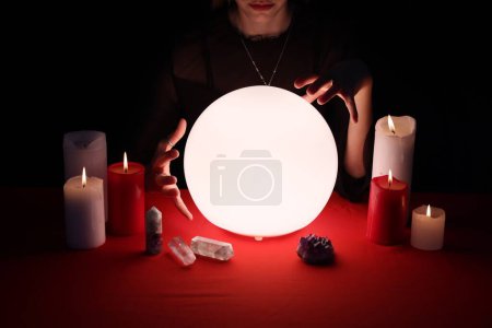 Photo for Soothsayer using glowing crystal ball to predict future  at table in darkness, closeup. Fortune telling - Royalty Free Image