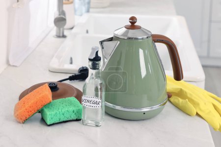Wasserkocher reinigen. Essigflasche, Schwämme und Gummihandschuh auf Arbeitsplatte in der Küche