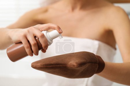 Foto de Auto-bronceado. Mujer que aplica el producto cosmético sobre el guante de bronceado en interiores, primer plano - Imagen libre de derechos
